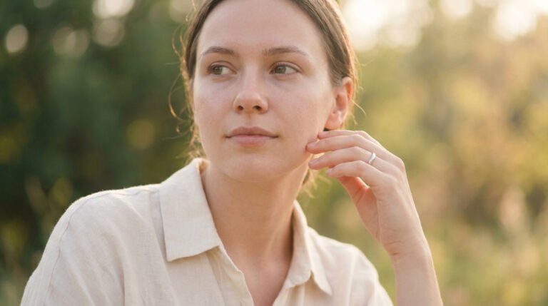 Portrait d'une jeune femme pensive touchant doucement sa joue dans un cadre naturel au soleil.